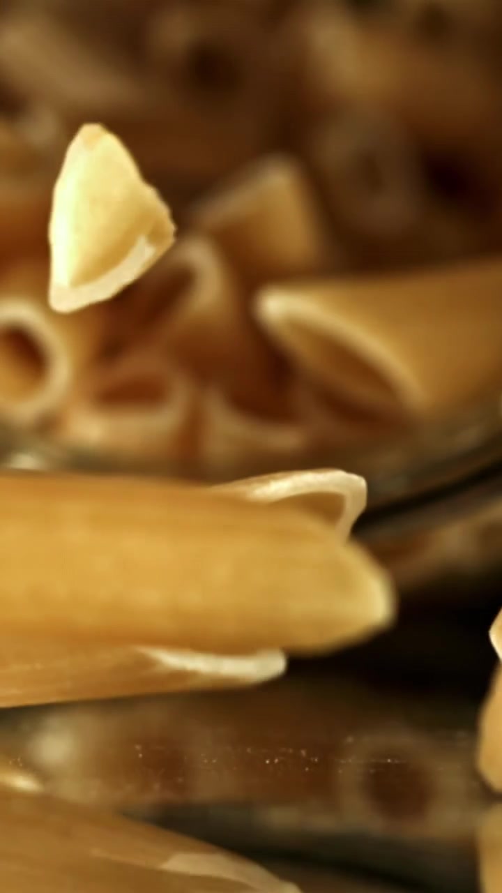 Dry Penne Pasta Falling onto a Reflective Surface in Slow Motion