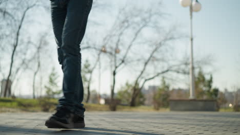 a close-up leg view of an adult carrying a child while walking down a street, with trees and light pole around and a blur view of a city behind him