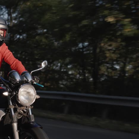 a man in a red jacket rides a motorcycle along the forest