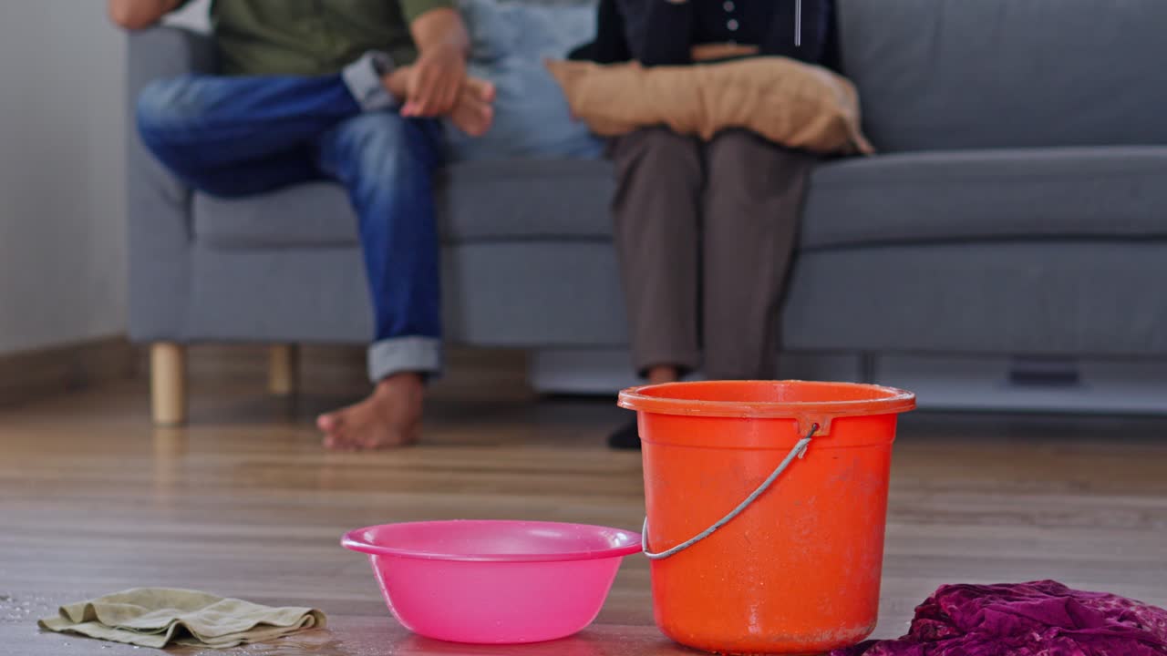 Conceito de vazamento no telhado de casa mostrando água pingando em recipientes enquanto um casal frustrado está sentado no sofá