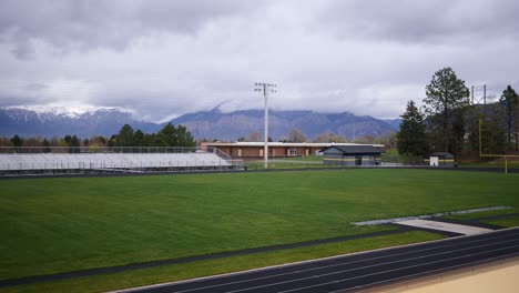 an empty football and track field on a cloudy day with a caucasian man with beard and long hair in bun running up and down stairs in and out of frame