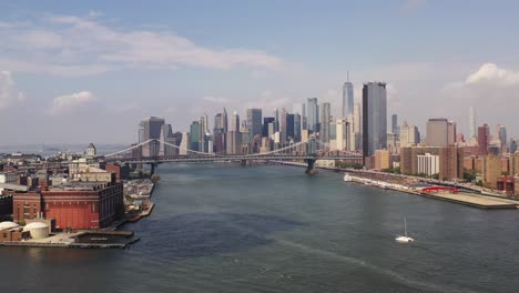 drone-flight-towards-Manhattan---Brooklyn-Bridge,-pan-left-with-a-single-white-catamaran-boat-in-the-East-River-below