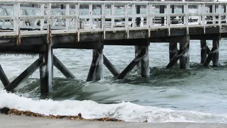 Wellen-Eines-Wintersturms-Stürzen-Unter-Einem-Dock-Ab-Und-Hinterlassen-Eiszapfen-Und-Schaum