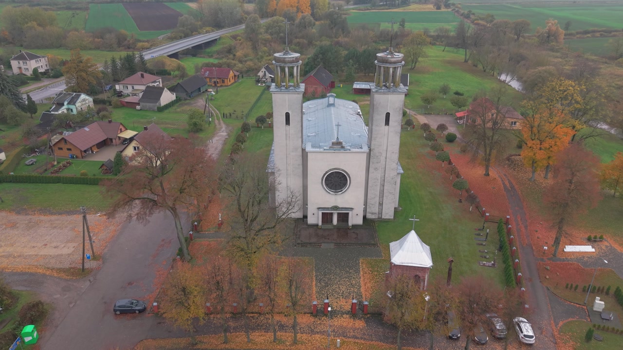 Drone footage capturing the serene beauty of Pilviškiai Holy Trinity Church in Lithuania. Surrounded by lush greenery and quaint village, perfect for depicting rural landscapes in autumn light.