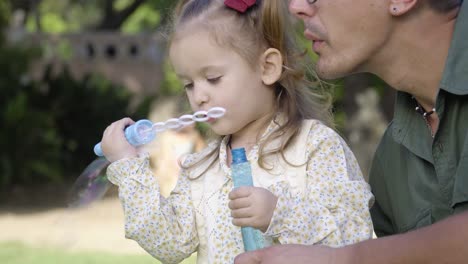 un joven padre ayuda a su adorable hija a jugar con burbujas en el parque de la ciudad