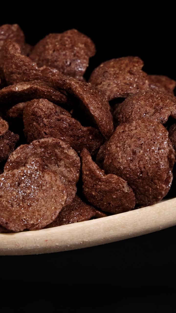 Chocolate cereal pieces tumble from a wooden spoon against a dark background, captured in slow motion