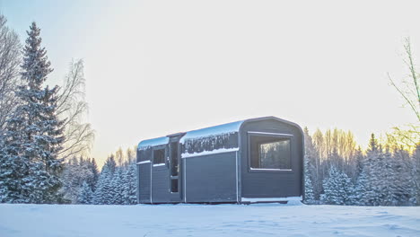 timelapse shot of rectangular wooden cabin surrounded by thick layer of snow during winter season on a cloudy day with trees in the background