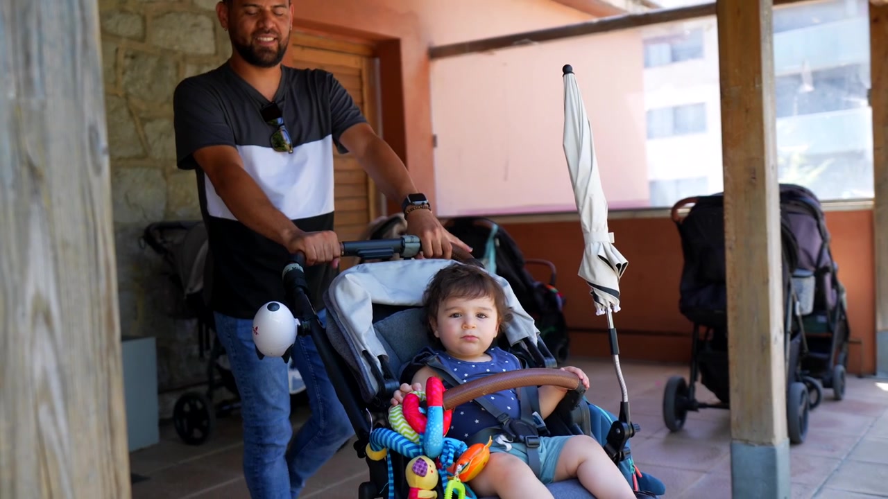 Padre felice che spinge il passeggino con il bambino all'aperto in una giornata di sole