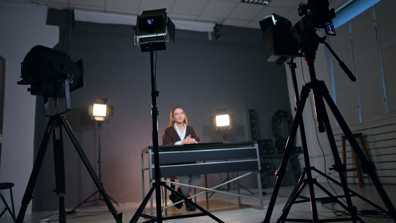 Backstage footage in the modern photo studio. Woman sits at desk in the lights of soffits speaking and gesturing.