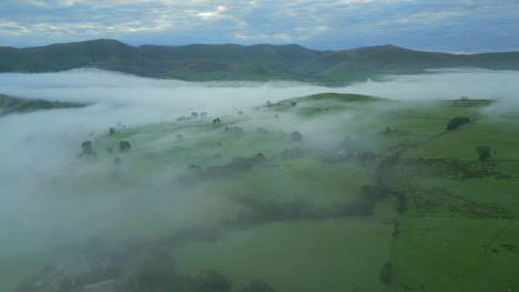 Flying-high-over-foggy-English-countryside-at-dawn-with-distant-mountains-and-patchwork-fields-at-sunrise