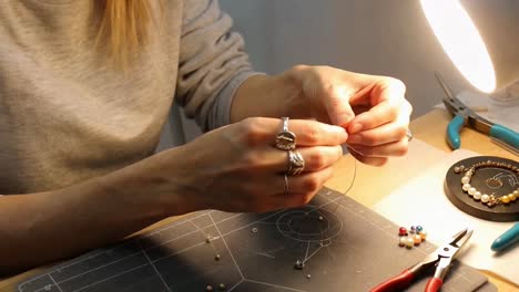 woman's hands crafting beaded jewelry with wire and pliers