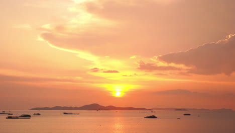 a dramatic orange and pink tropical sunset turn the ocean waters filled with small boats and a mountainous island in the distance