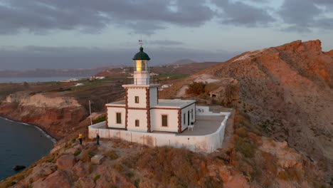 aerial backwards revealing shot of akrotiri lighthouse in santorini, greece during dusk