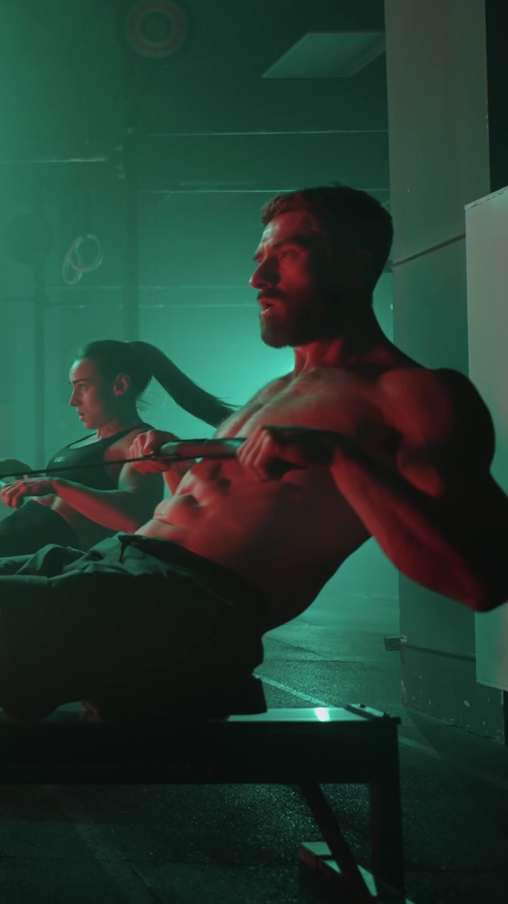Uomo e donna che si allenano sui vogatori in una palestra illuminata di verde