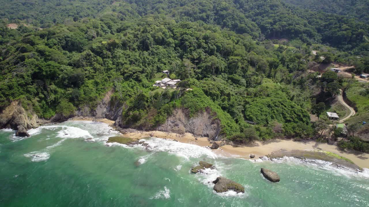 A stunning bird’s-eye view captured by a drone of a coastline with a road and forested mountains, and the Caribbean Sea with turquoise water and waves.