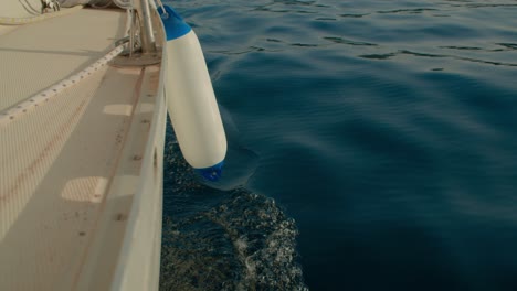 Sea-water-splashing-against-sailing-sailboat,-fender-on-side,-handheld,-day