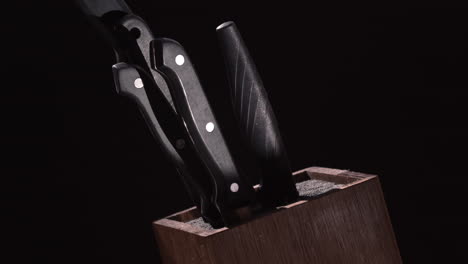 set of kitchen knives with black handle placed on wooden knife holder isolated on black background - closeup shot