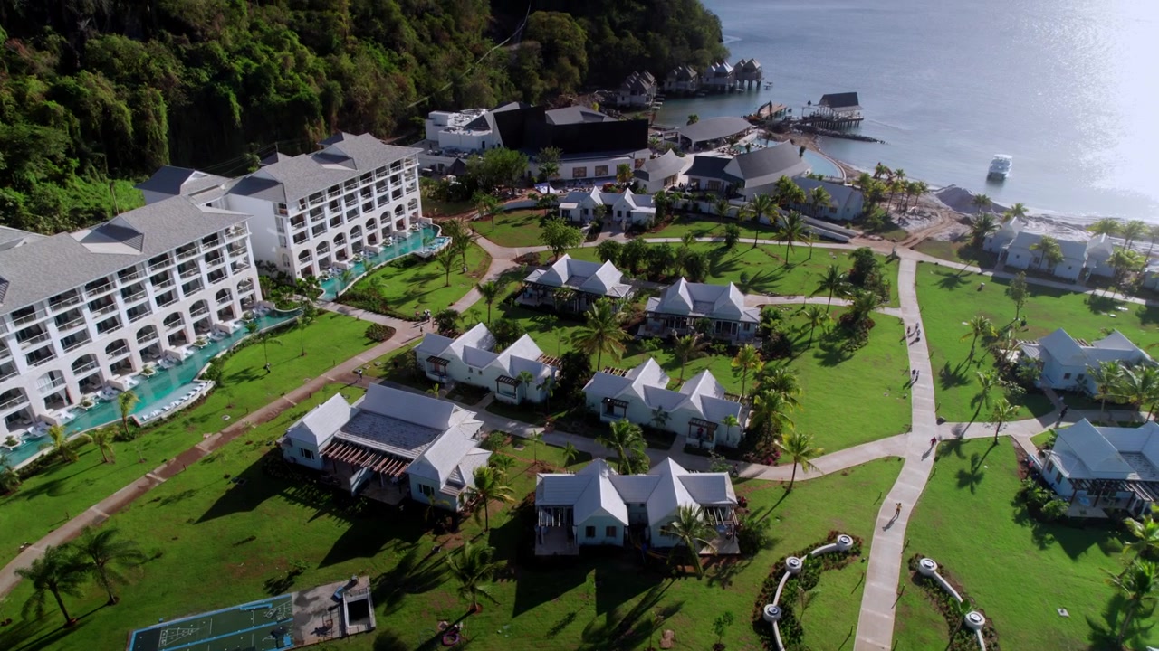 Drone pullback from luxury hotel suites with swim-up pools, transitioning over manicured tropical grounds to reveal a cluster of boutique villas and the surrounding coastal resort infrastructure