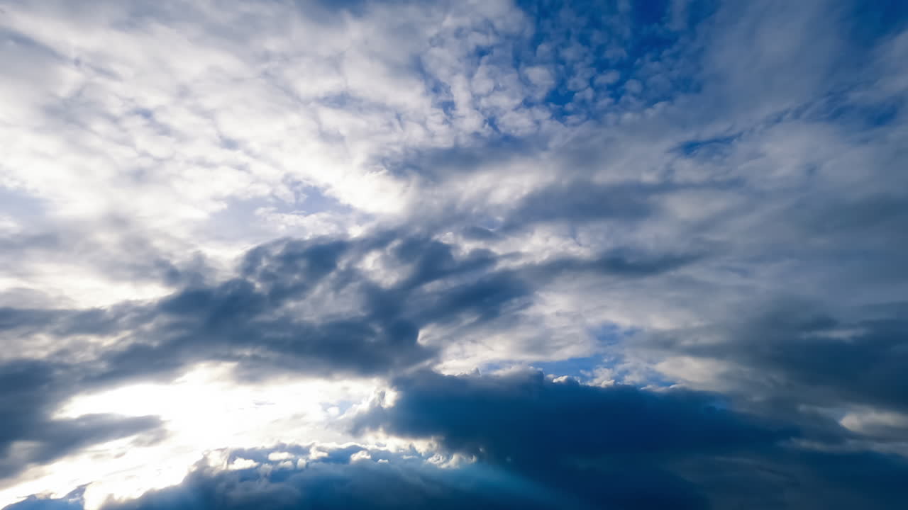 Grey cloudscape shading the sun. Blue skies are covered by the dramatic clouds. Low angle view. Timelapse.