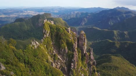 Descending-aerial-shot-of-Mountain-landscape-featuring-a-jagged-rock-formation-in-Coromandel,-New-Zealand