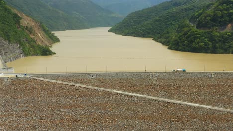 Camera-flies-backwards-revealing-the-Hidroituango-dam-as-a-truck-drives-over-it,-located-on-the-Cauca-river-in-Ituango,-Antioquia,-Colombia