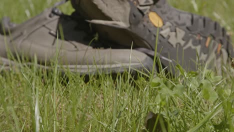 Slow-dolly-in-over-blades-of-grass-toward-discarded-hiking-shoes-in-nature