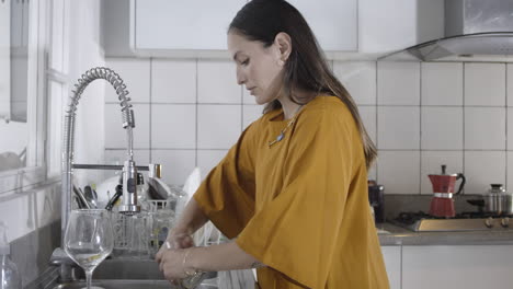 hermosa latina lavando platos en la cocina blanca