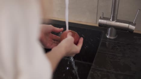 Woman-hands-washing-apple-in-the-kitchen-sink