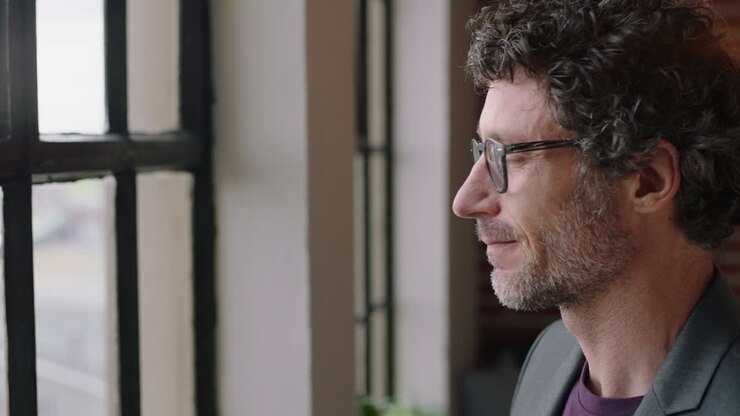 attraente uomo d'affari caucasico che guarda fuori dalla finestra progetta il futuro sorridendo imprenditore felice che gode di uno stile di vita di successo rilassandosi a casa indossando occhiali