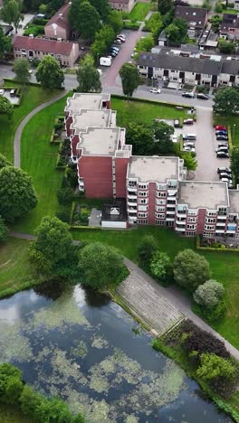 aerial view of a residential area with apartment buildings, a park, pond, and parking lot