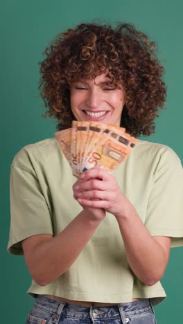 cheerful woman showing euro banknotes in green studio. vertical footage