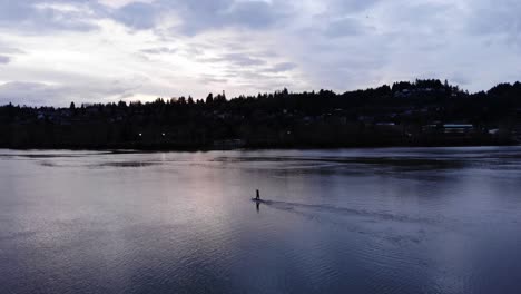 Amplia-Toma-Panorámica-Lenta-Izquierda-Silueta-De-Un-Paddle-Boarder-Viajando-A-Lo-Largo-Del-Río-Willamette,-Portland,-Oregon