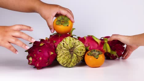 hands interact with dragon fruit and persimmons