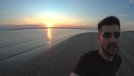 hombre en primera persona corriendo en la playa con la puesta de sol detrás