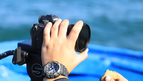 A-man-is-wiping-a-camera-lens-while-on-a-boat