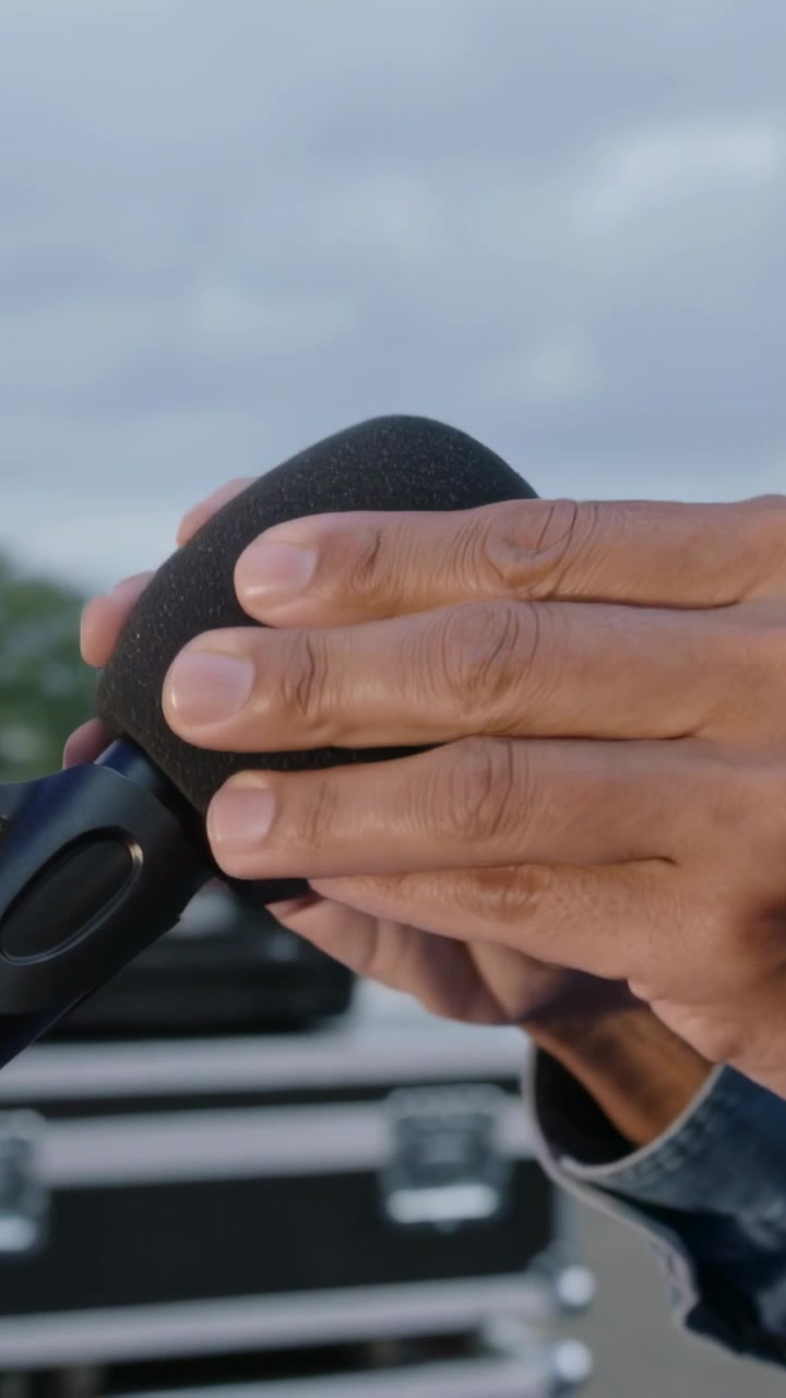Video verticale: Mani che si allungano per applicare la spugna su un microfono sul palco, preparandolo per l'uso, manica di jeans
