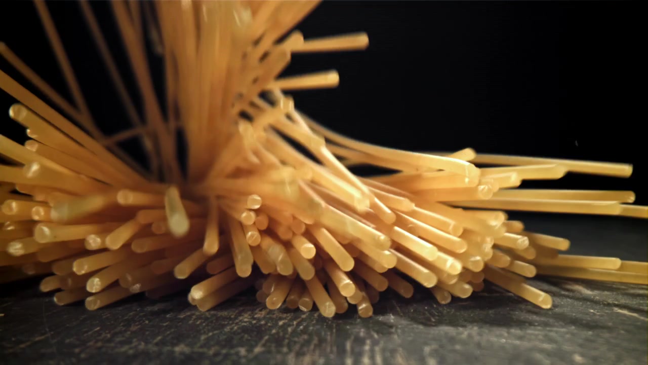 Spageti kering jatuh dalam gerakan lambat ke permukaan gelap.