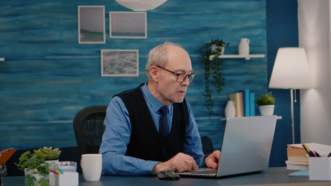 Old freelancer typing on laptop sitting in living room working remote