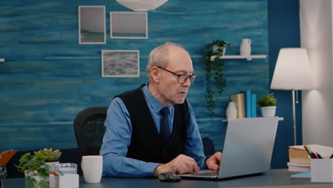 viejo trabajador independiente escribiendo en una computadora portátil sentado en la sala de estar trabajando remotamente