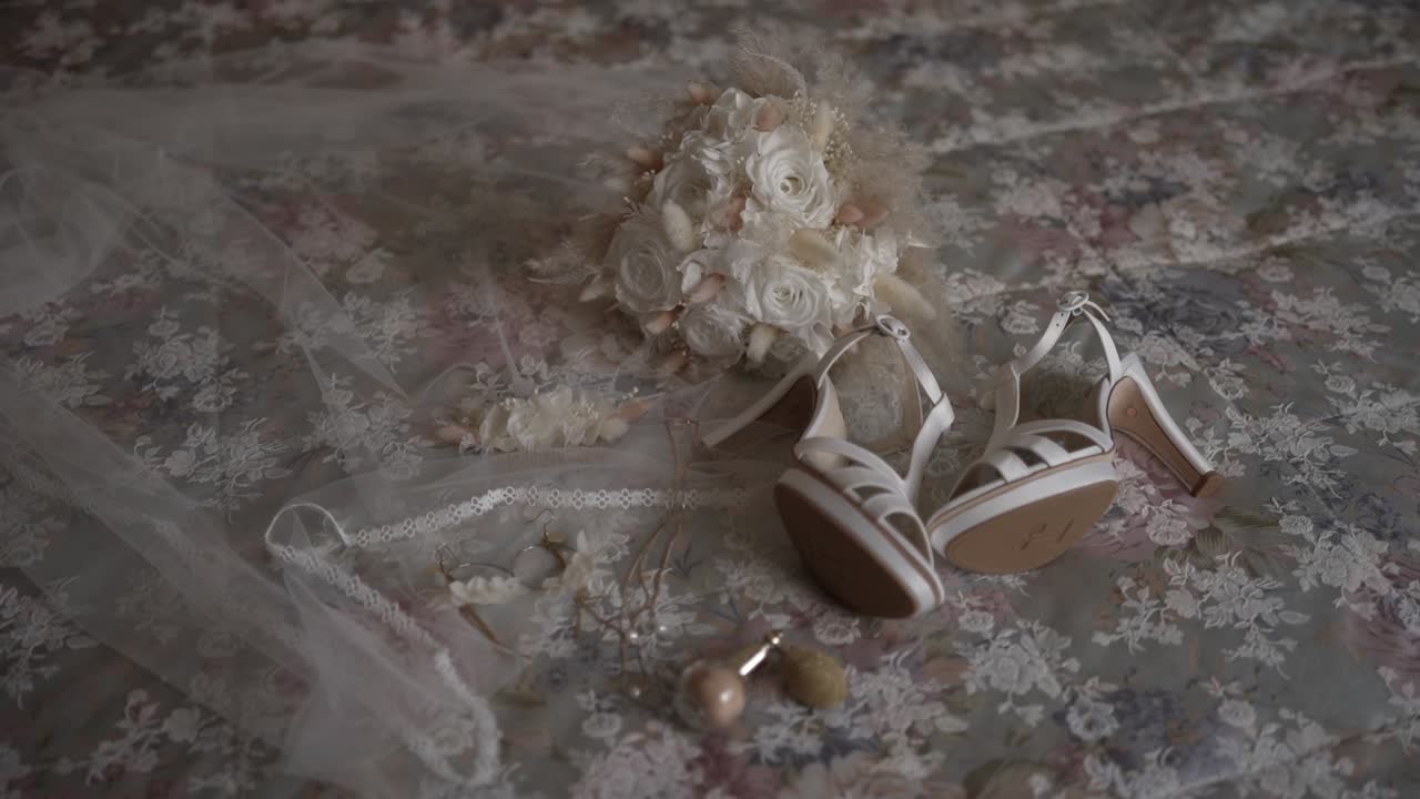 White bridal heels, floral bouquet, lace veil, and jewelry on floral patterned bedspread