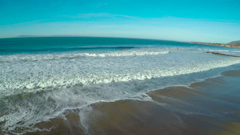 an aerial over a generic beach heading out to the ocean with large waves and surf breaking