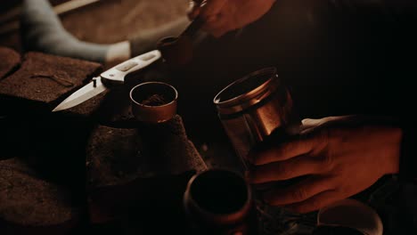 campfire coffee: young homeless man putting coffee grounds into the metal filter of the old beat up moka pot he uses to brew his favourite baverage