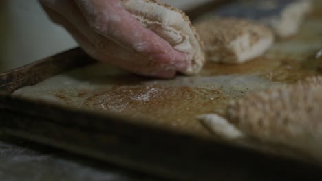 bread dough blank with sesame is carefully placed on a baking tray by a baker