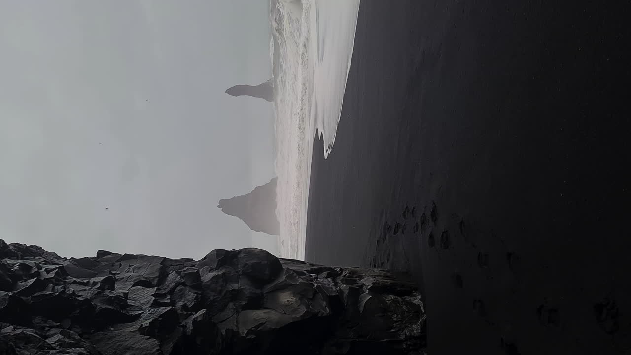 video vertical, playa de arena negra y la pintoresca costa de islandia en un día de lluvia oscura