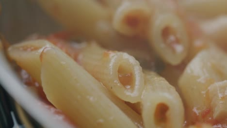 stirring hot penne pasta with tomato sauce in pan during cooking