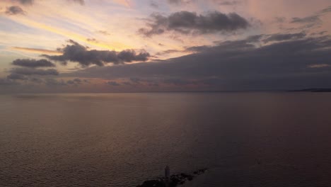 Aerial-view-of-dusk-sky,-aerial-drone-backward-reveals-offshore-lighthouse