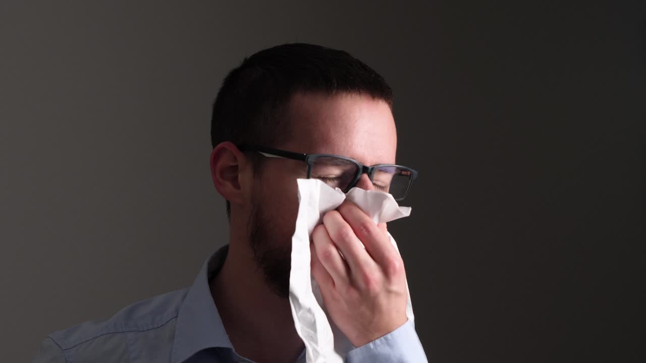 joven enfermo con gafas estornuda fuertemente en un papel tisú - cámara lenta