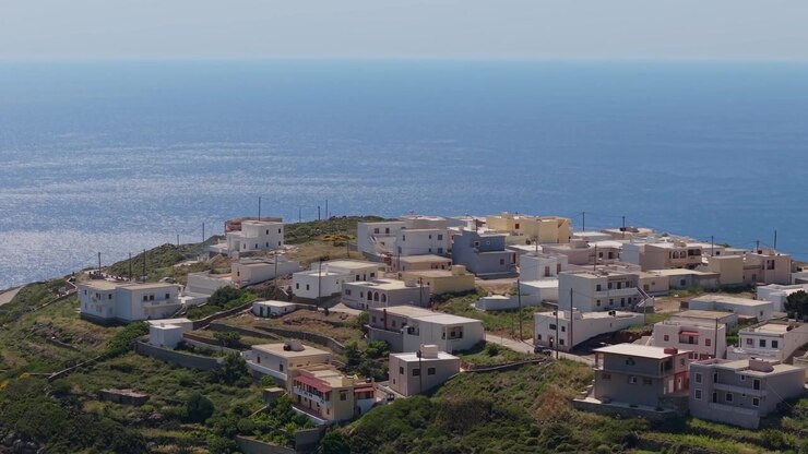 Ripresa aerea orbitale che mostra il villaggio di Spoa arroccato in alto sopra l'isola, con viste panoramiche del terreno aspro di Karpathos e del profondo blu del Mar Egeo.