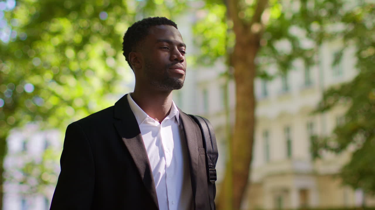 joven empresario con mochila caminando a trabajar en la oficina a lo largo de la calle arbolada en el distrito financiero de la ciudad de londres, reino unido