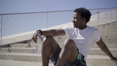 smiling sporty young man sitting on stairs and drinking water.